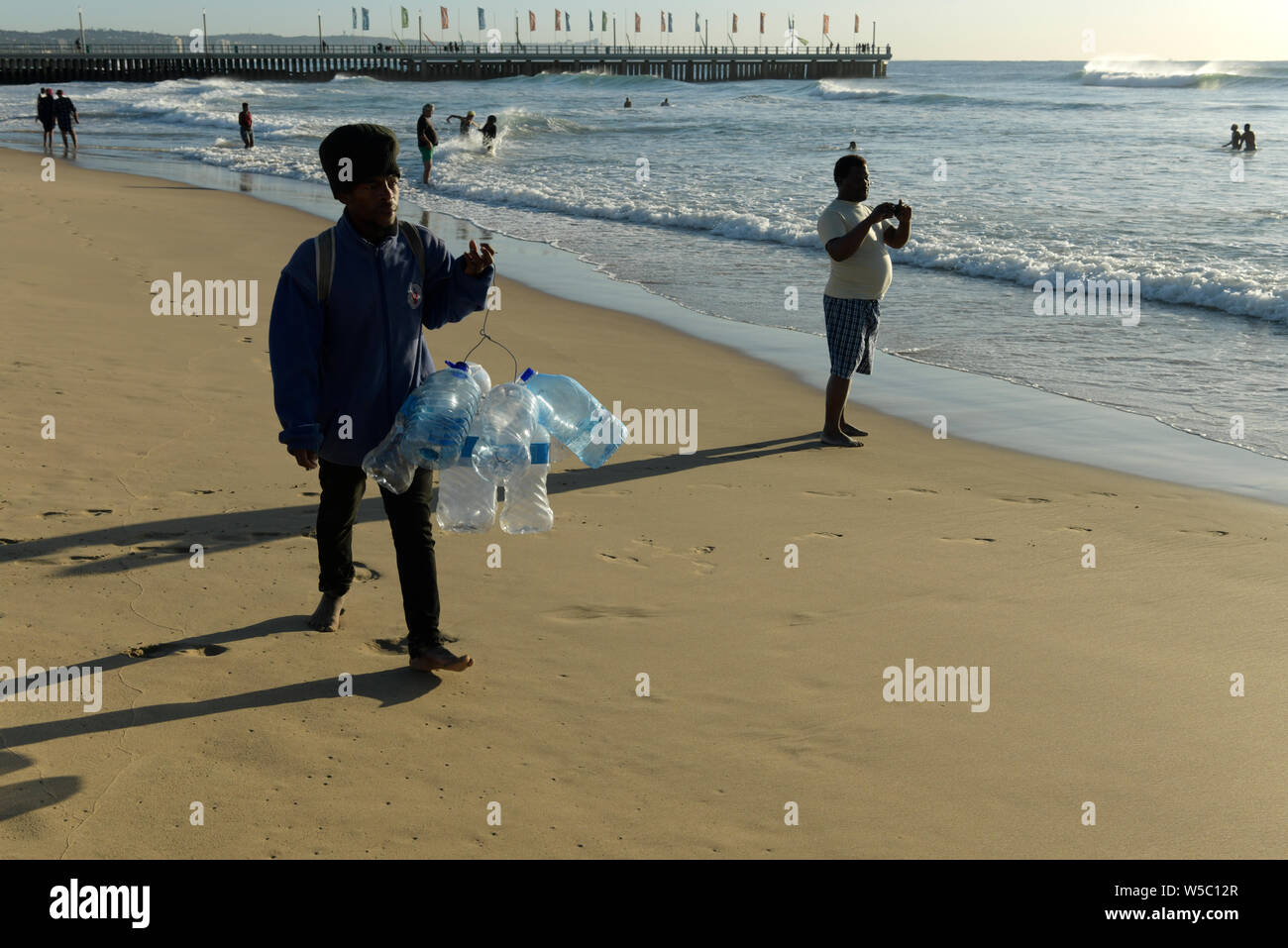 Durban, KwaZulu-Natal, South Africa, adult man, plastic bottle seller, collection of sea water for belief medicine, candid, people, beach, landscape Stock Photo