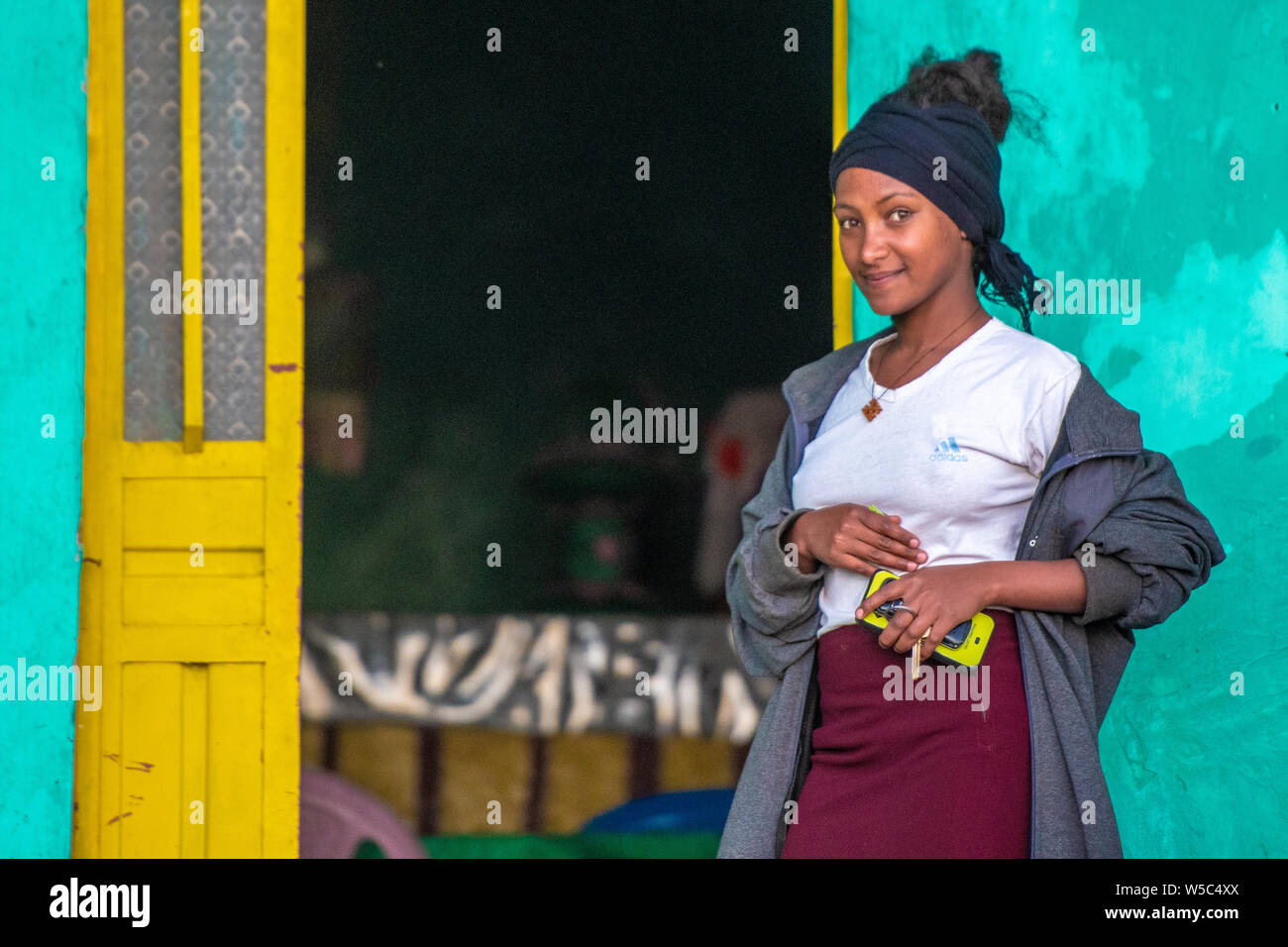 A young woman poses outside of her house for a photograph, Debre Berhan