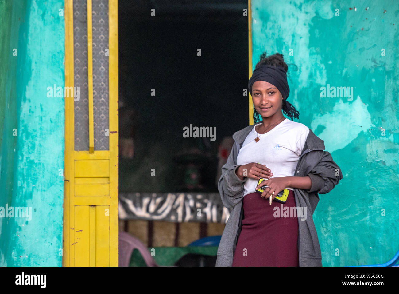 A young woman poses outside of her house for a photograph, Debre Berhan