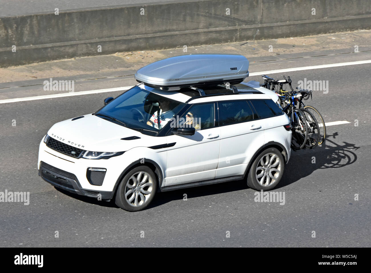 White Range Rover car view from above looking down on roof box & rear mounted bike cycle rack on m25 motorway concrete crash barrier beyond England UK Stock Photo