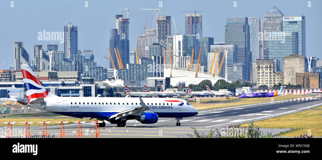British Airways plane moving onto London City Airport runway for taking off landmark skyscraper buildings in cityscape skyline Canary Wharf beyond UK Stock Photo