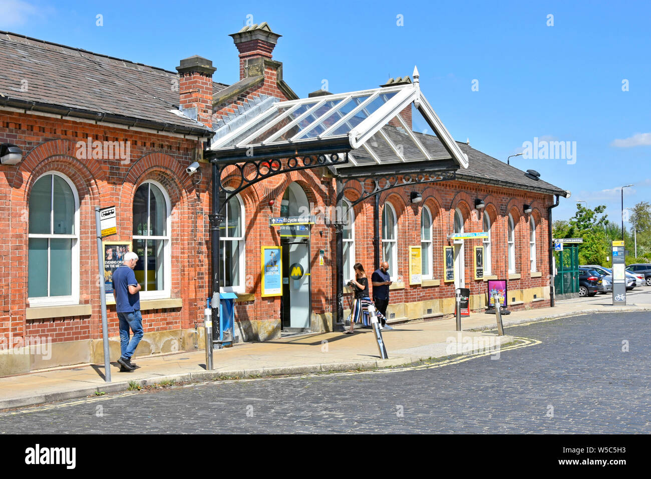People outside Ormskirk Merseyrail Victorian old listed public transport railway station building & bus stop in cobbled street Lancashire England UK Stock Photo