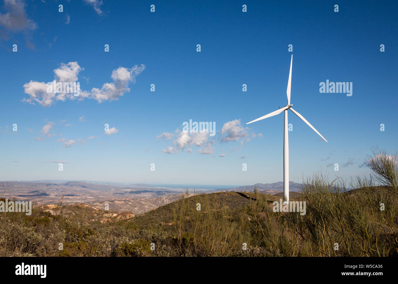 A landscape view in the desert of Sierra Alhamilla in Andalusia Spain, with a wind turbine and a blue sky with white clouds Stock Photo