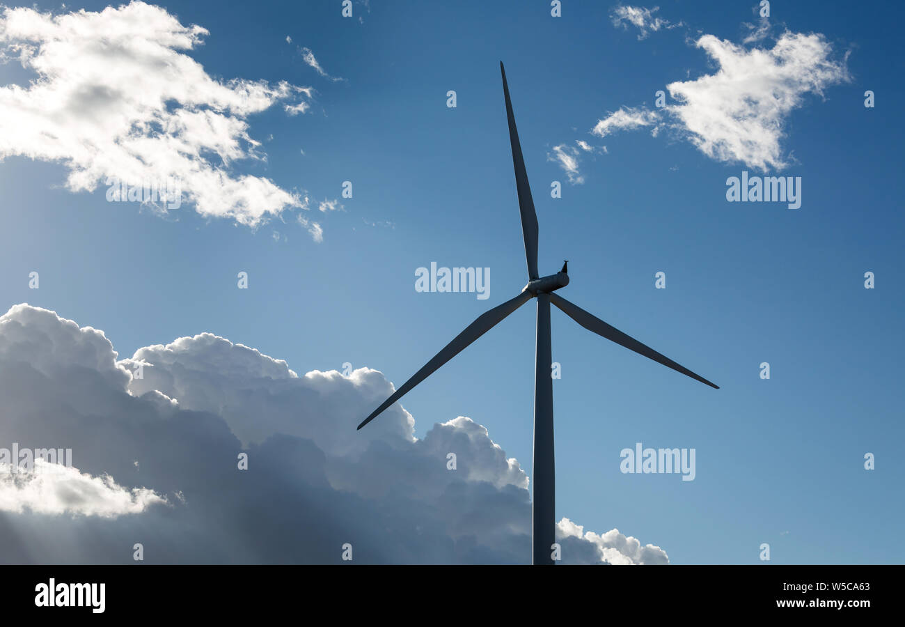A wind turbine against a blue sky with white clouds Stock Photo