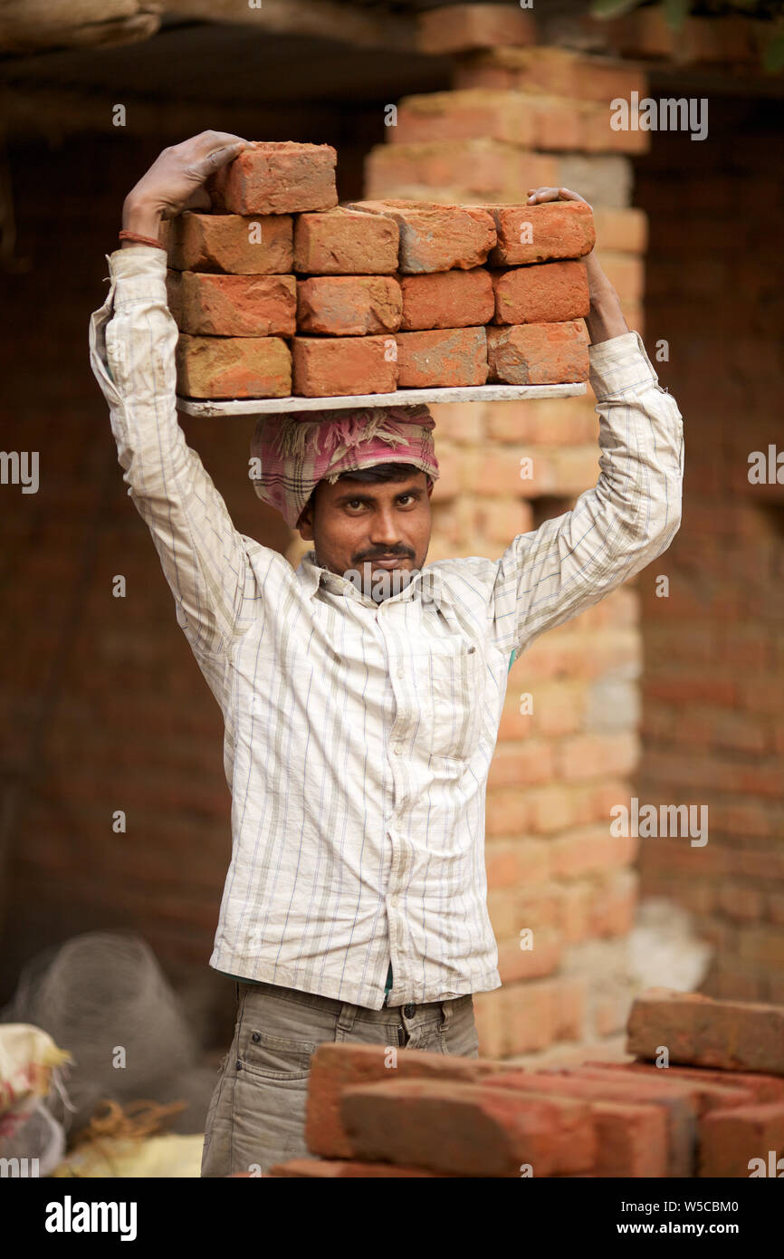 Manual worker carrying bricks on his head at construction site Stock