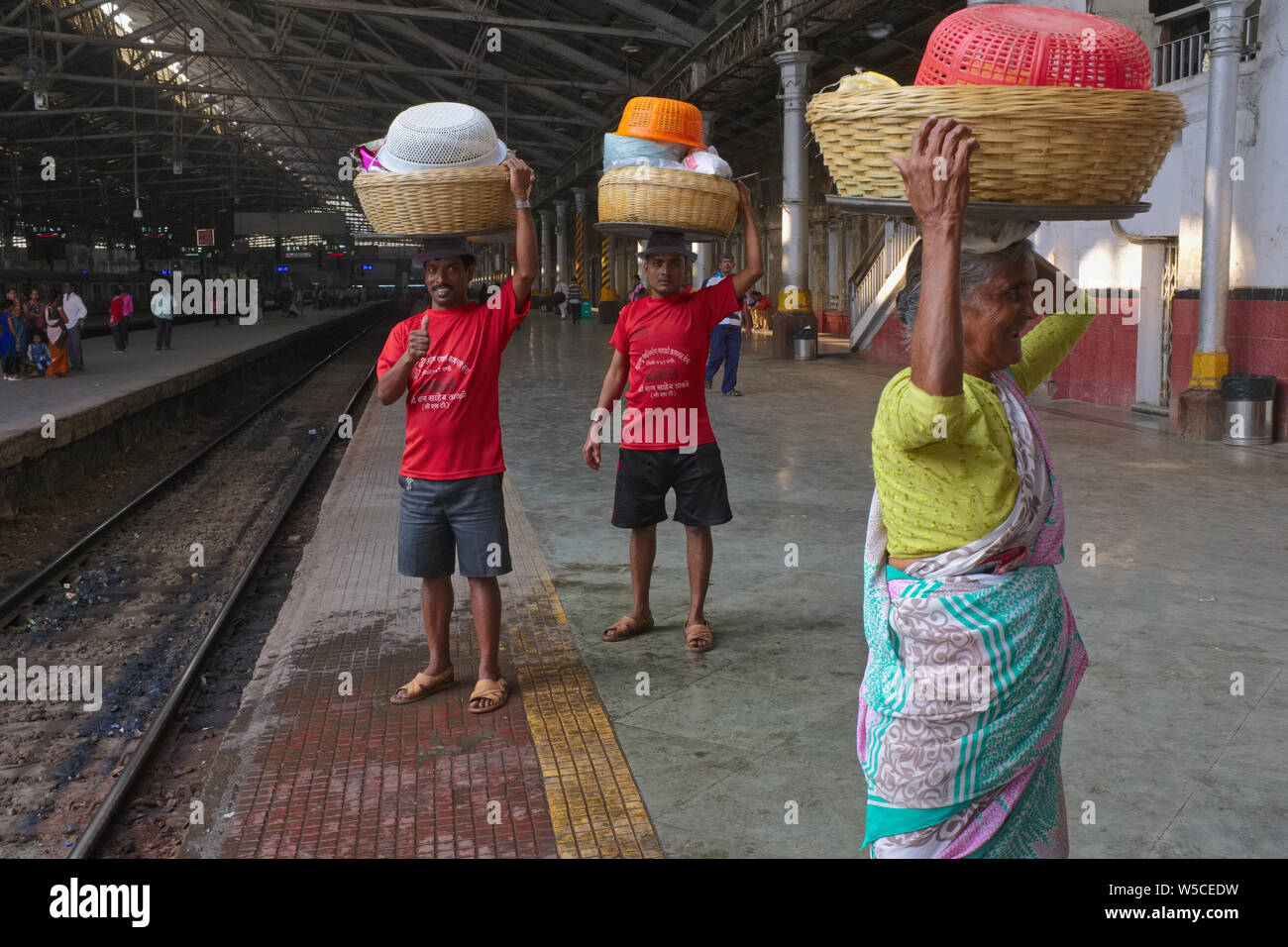 Porters at Chhatrapati Shivaji Maharaj Terminus (CSMT) in Mumbai, India, carrying baskets with fish on their heads to deliver to an incoming train Stock Photo