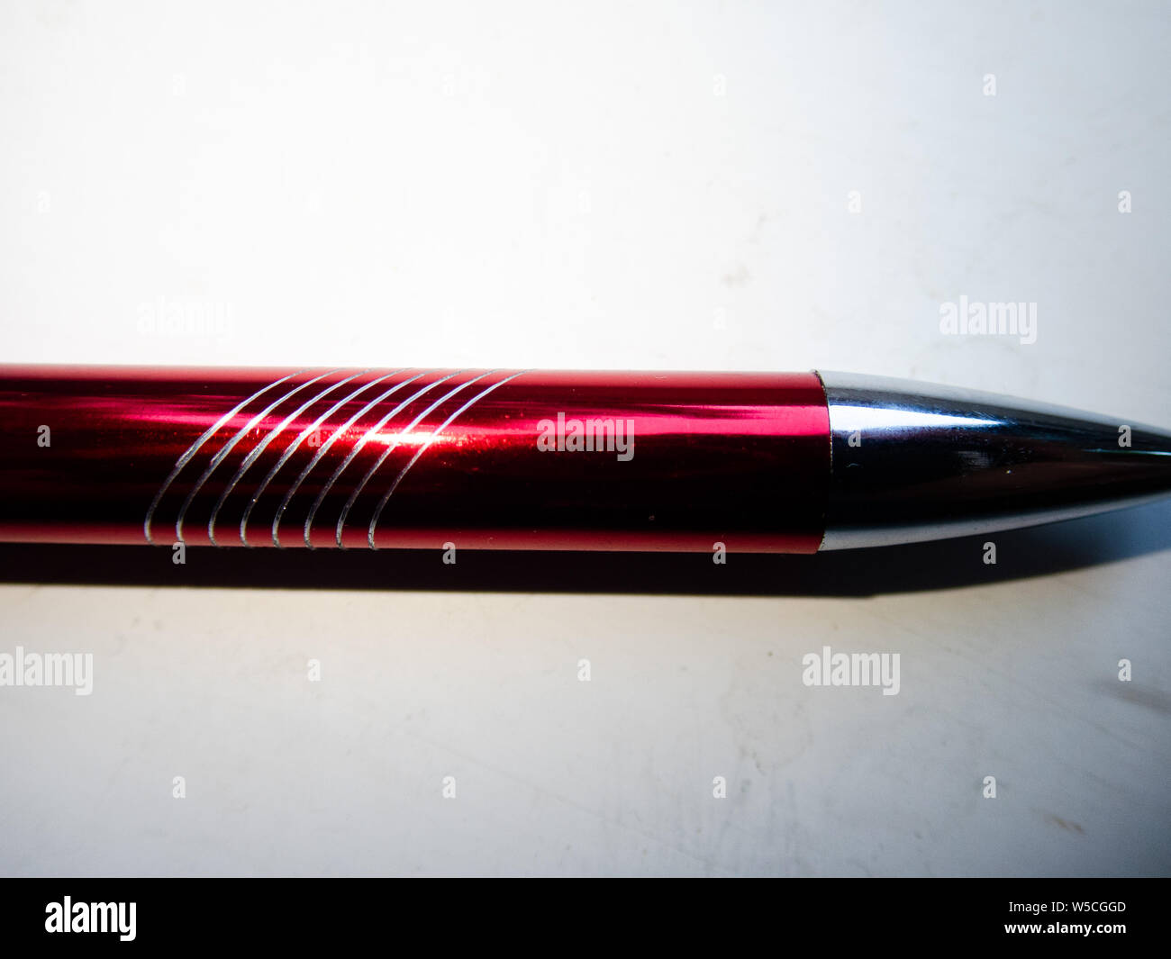 Cool background - macro of a metallic red pen with some white lines on it, transition from dark to bright Stock Photo
