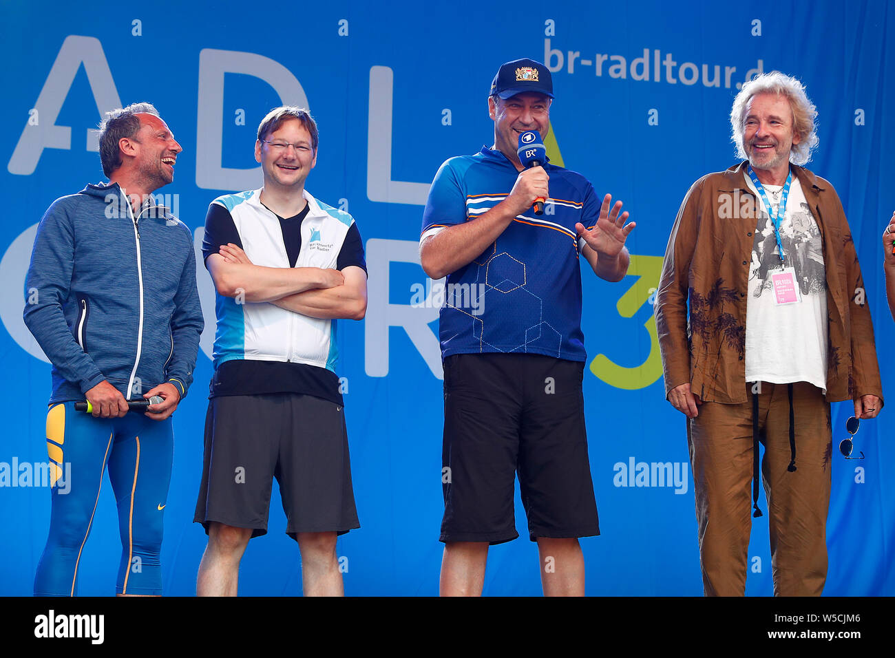 Bad Staffelstein, Germany. 28th July, 2019. Entertainer Thomas Gottschalk (r-l), Markus Söder (CSU), Minister President of the Free State of Bavaria, Hans Reichhart (CSU), Minister of State for Housing, Construction and Transport, and Thorsten Glauber (Free Voters), Minister of State for the Environment and Consumer Protection, will be on stage at the opening of the 30th BR Cycling Tour. Credit: Peter Kolb/dpa/Alamy Live News Stock Photo
