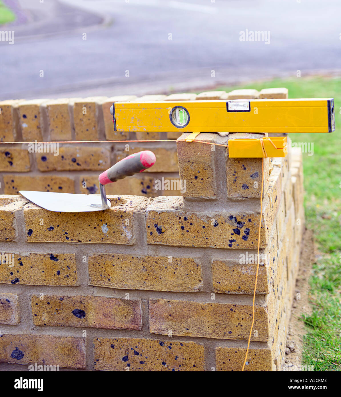 bricklayers trowel, spirit level, block line and tingle on a partially built brick plant container. Stock Photo