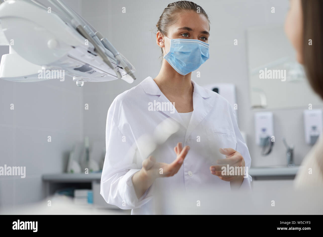 Portrait of young female dentist wearing protective mask consulting patient in clinic, copy space Stock Photo