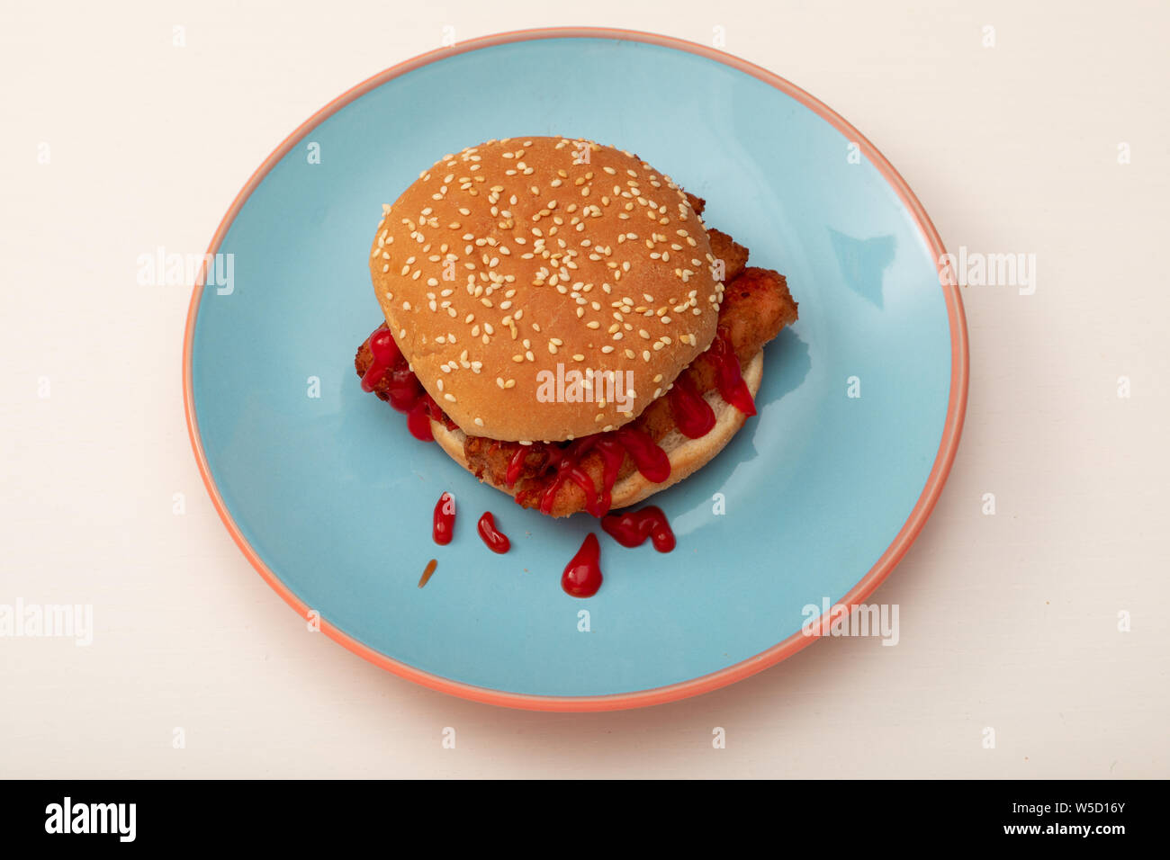 Vegan sausage sandwich with tomato ketchup on a seeded bun on a blue plate Stock Photo