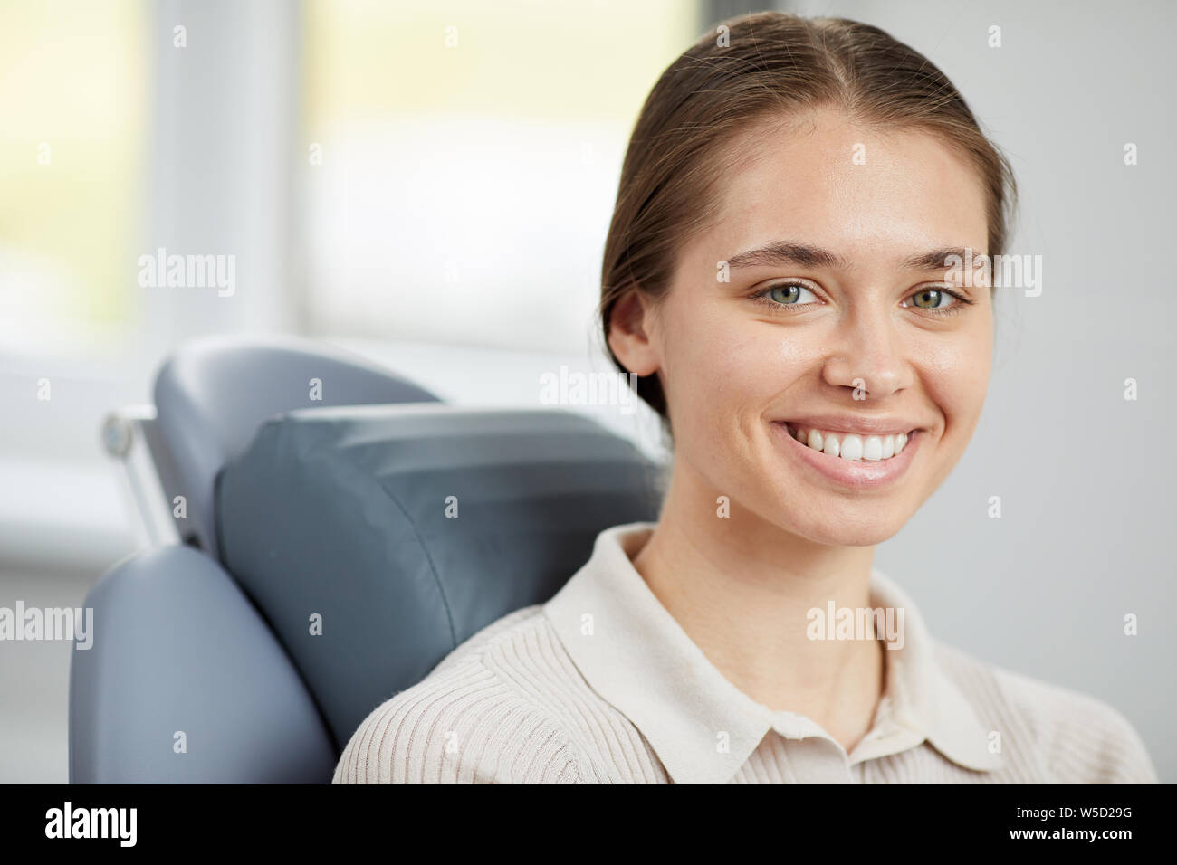 Head and shoulders portrait of pretty young woman smiling at camera and showing perfect white teeth while sitting in dental chair, copy space Stock Photo
