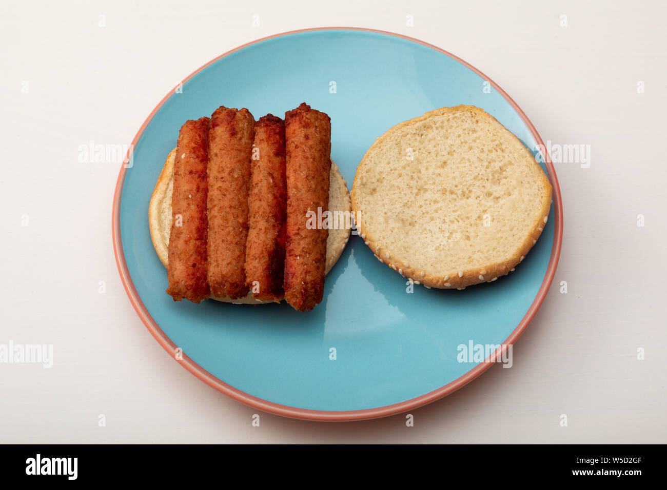 Vegan sausage sandwich on a seeded bun on a blue plate Stock Photo