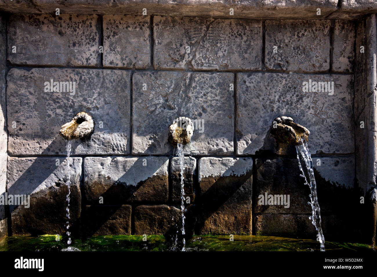 Three stone taps from which water flows. The water is clean and clear to drink. Cranes are made in the wall of an old building. Stock Photo