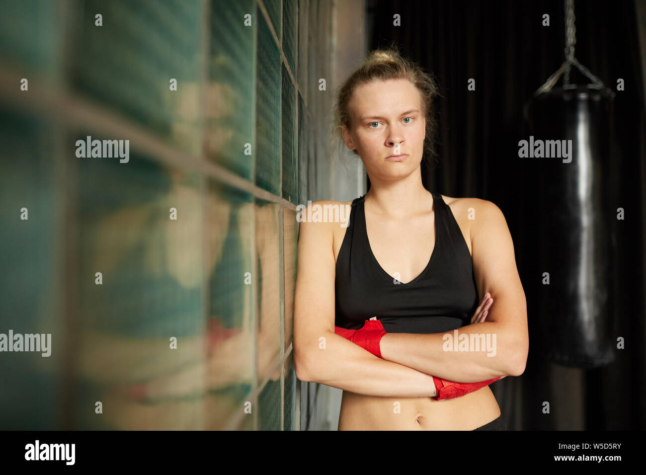 Waist up portrait of tough sportswoman looking at camera while leaning on glass wall in sports club, copy space Stock Photo