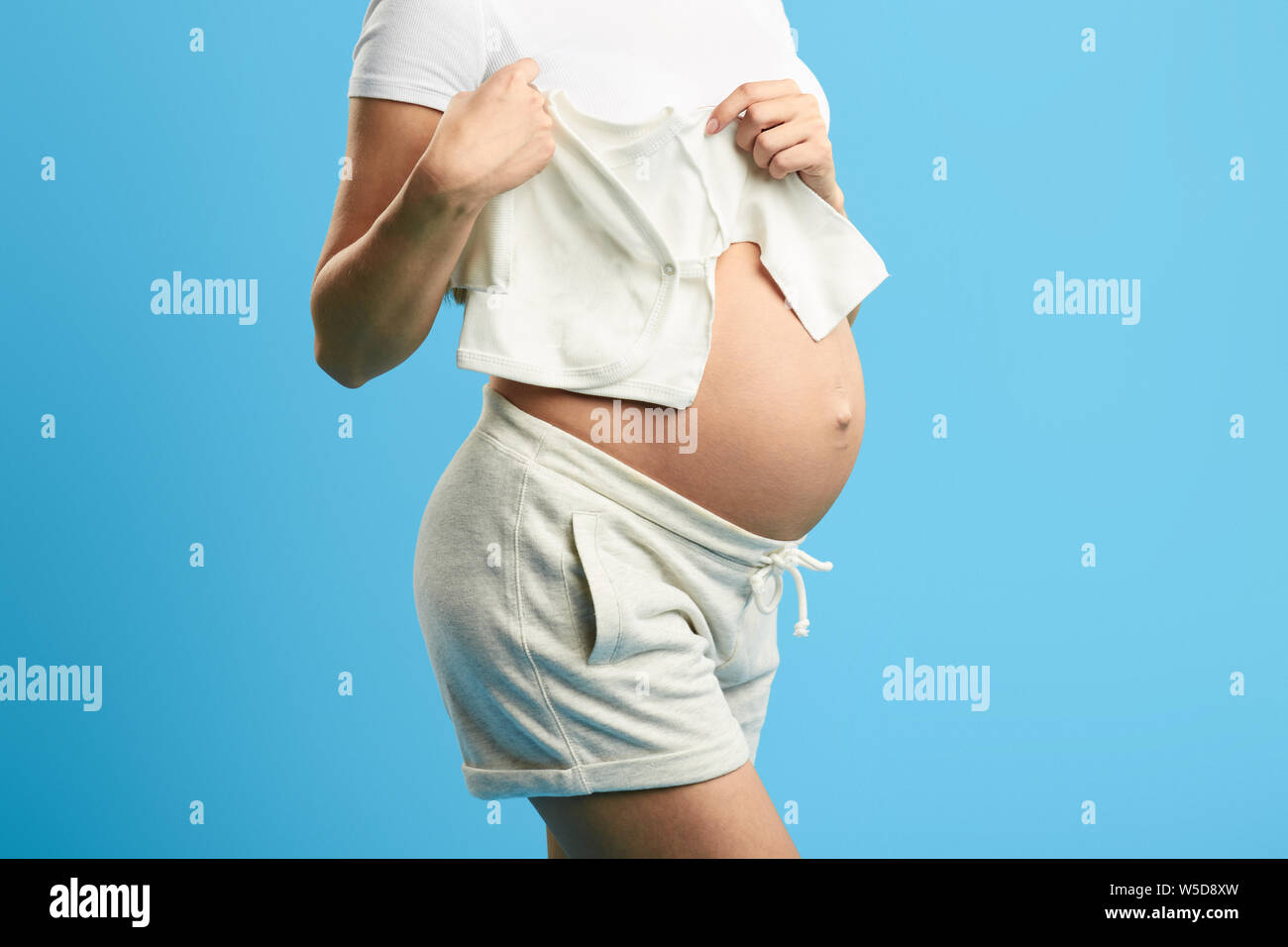 Close Up Cropped Photo Pregnant Woman Holding Baby S Clothes On Her Big Belly Isolated Blue Background Studio Shot Heir Successor Stock Photo Alamy