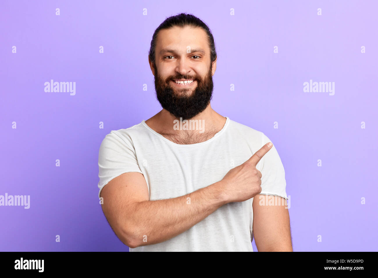 positive bearded guy pointing aside with finger .place for text, copy space. isolated blue background. studio shot Stock Photo
