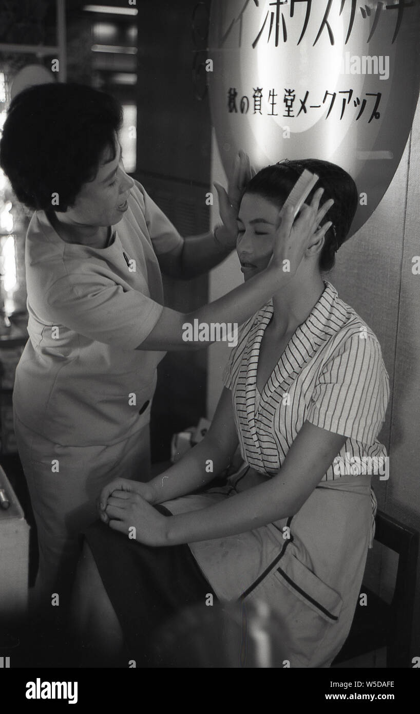 [ 1950s Japan - Shiseido Make-Up Demonstration ] —   A Shiseido (資生堂) make-up artist touches the face of a young woman during a make-up demonstration at a Tokyo department store, 1958 (Showa 33). Stock Photo
