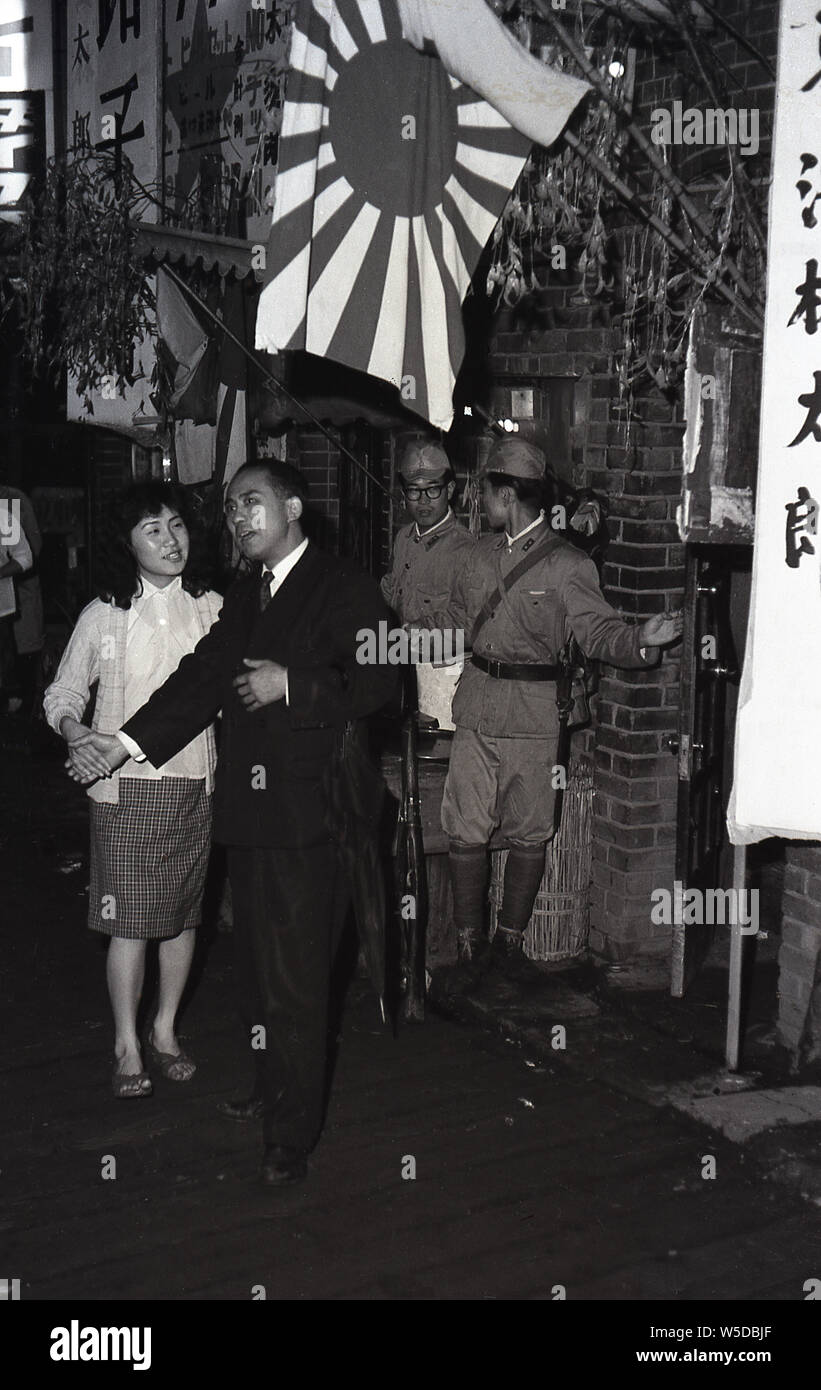 [ 1960s Japan - Tokyo Night Club ] —   An office worker and his companion, most likely a hostess, in front of a war themed night club in Tokyo, 1960 (Showa 35). Stock Photo