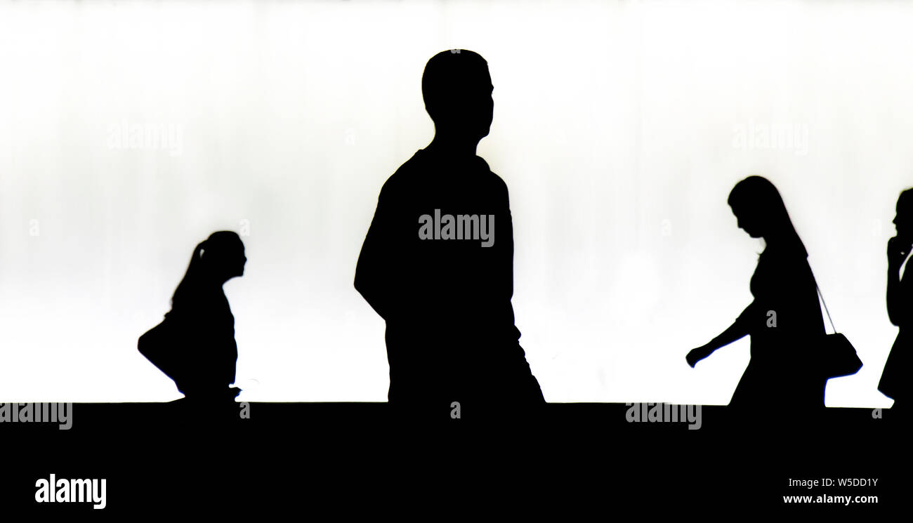 Belgrade, Serbia - July 23, 2019: Silhouettes of one young man walking alone in the night and young women passing by behind him, in  black and white Stock Photo