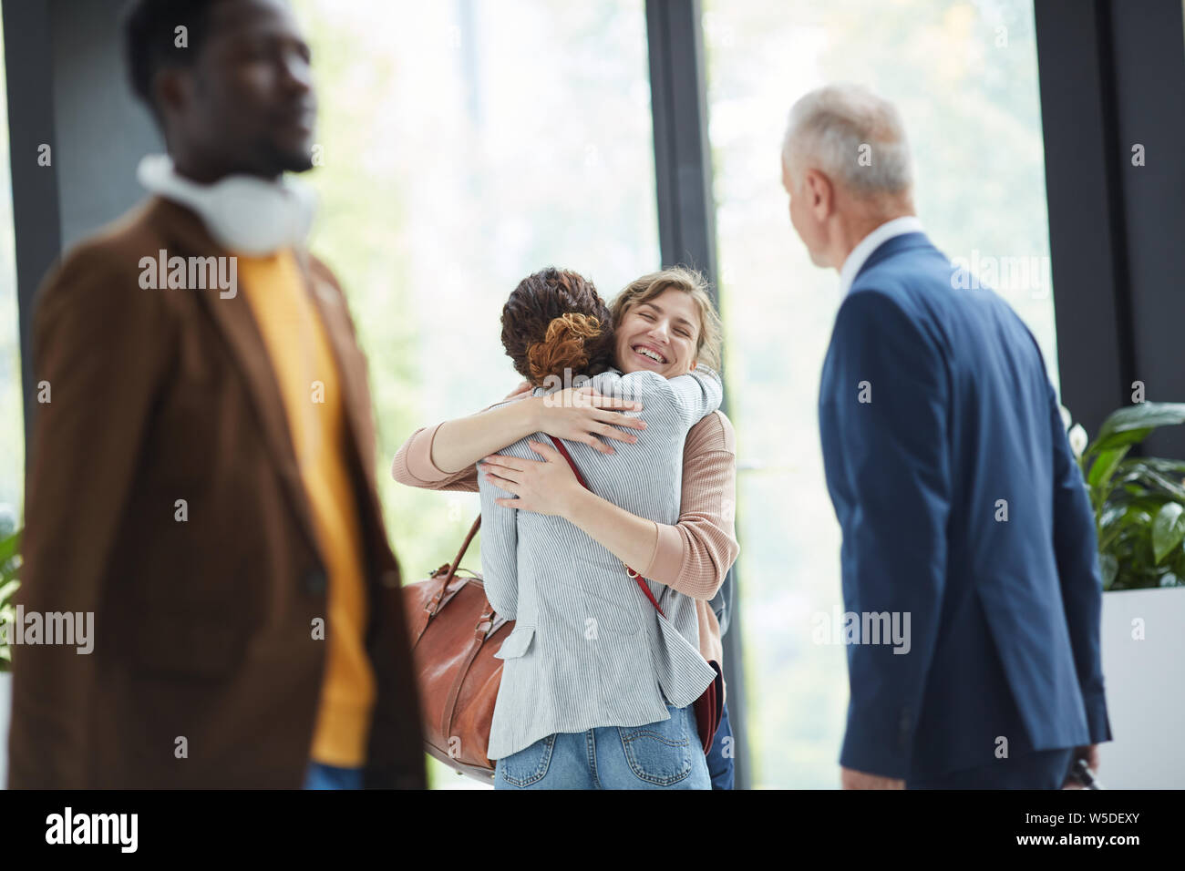 Happy excited young friends standing in hall and hugging in airport after long separation Stock Photo
