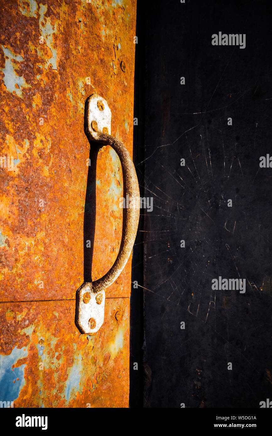 Bright sun on  a rusty metal door with rust covered handle and a spiders web,  near Consett, County Durham, England, UK Stock Photo