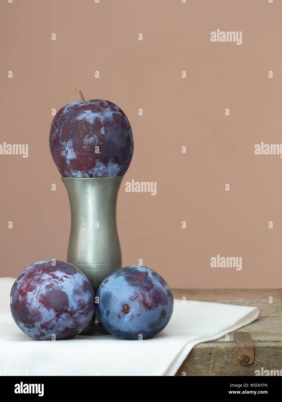 Three dark red, purple plums one on vase pedestal. Stock Photo