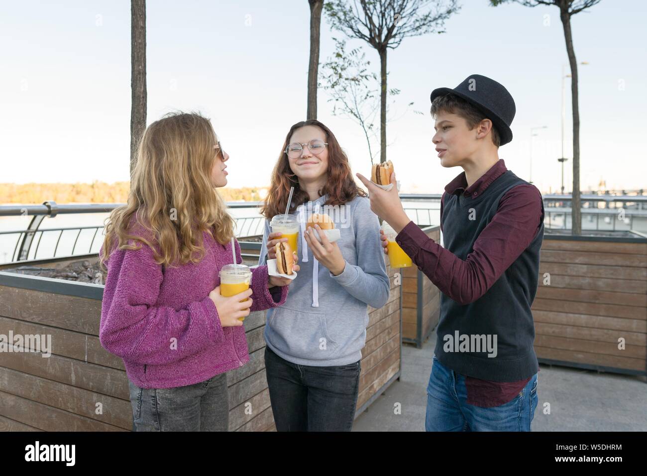 Teenagers eat street food, friends boy and two girls on city street