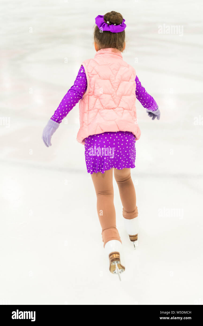 Little girl practicing figure skating in a purple dress with crystals