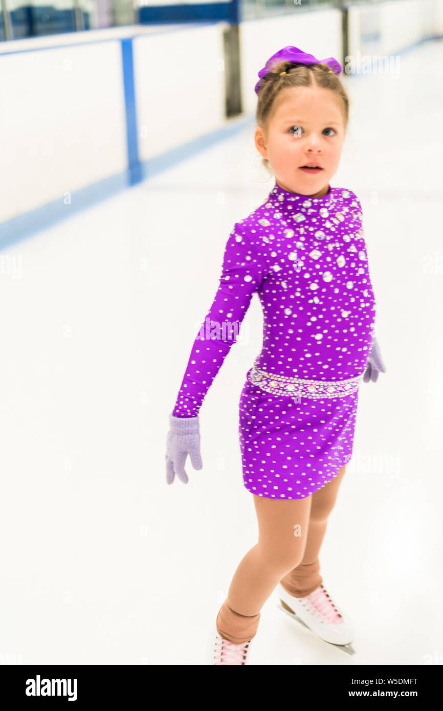 Little girl practicing figure skating in a purple dress with crystals