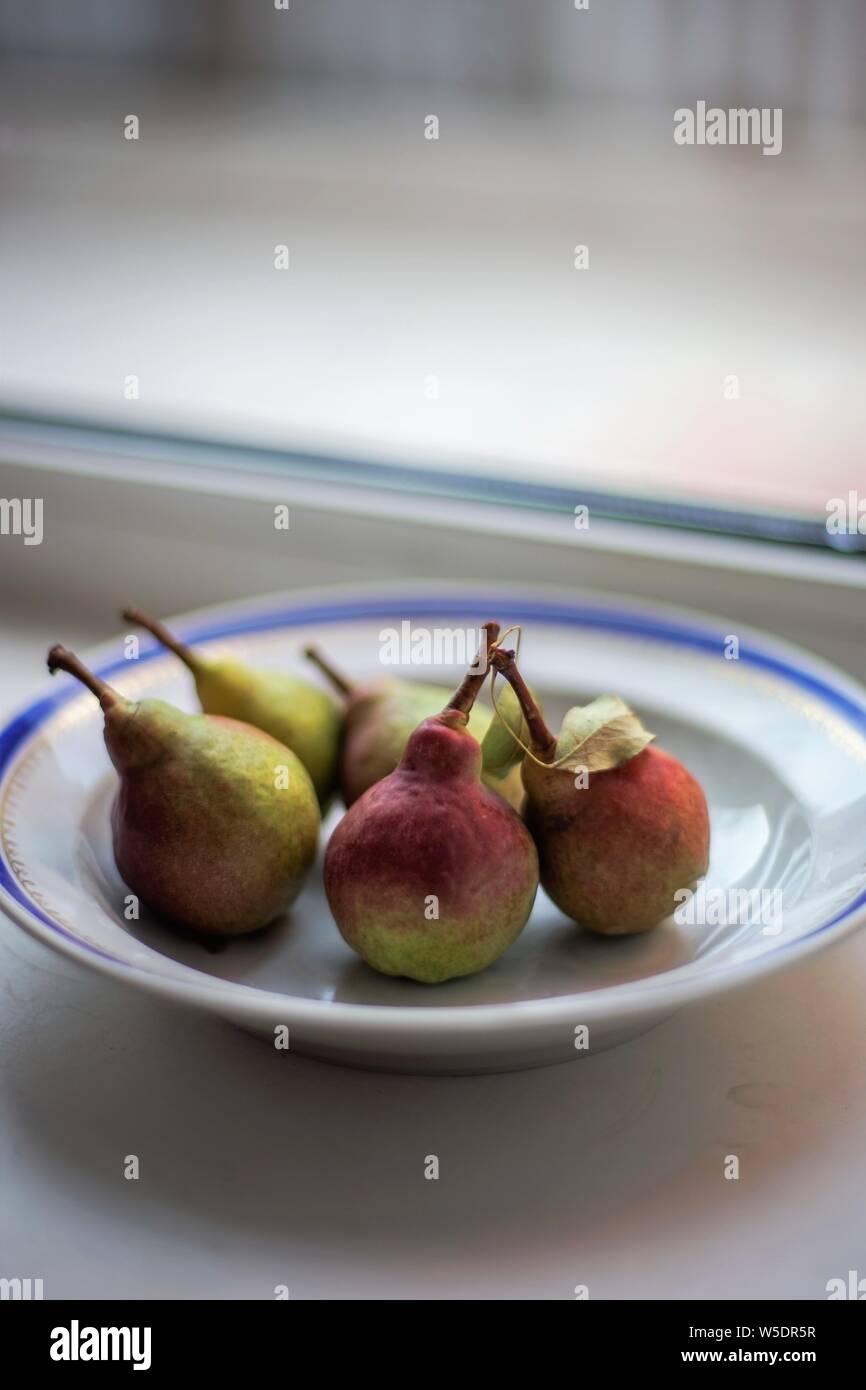 five ripe pears in a plate on the windowsill Stock Photo