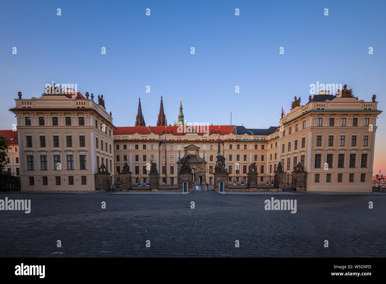 Entrance with forecourt to Prague Castle from Hradschin Square. Historic building with fence and Titans sculptures in the evening with blue sky Stock Photo