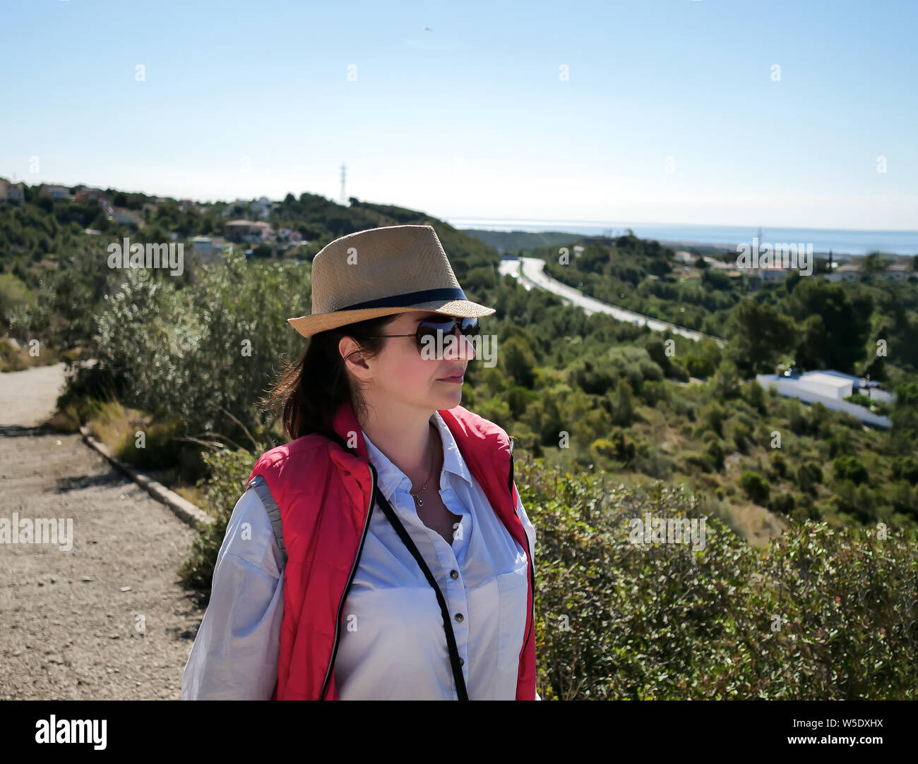 Pretty brunette with a hat and glasses looks at the surrounding countryside Stock Photo