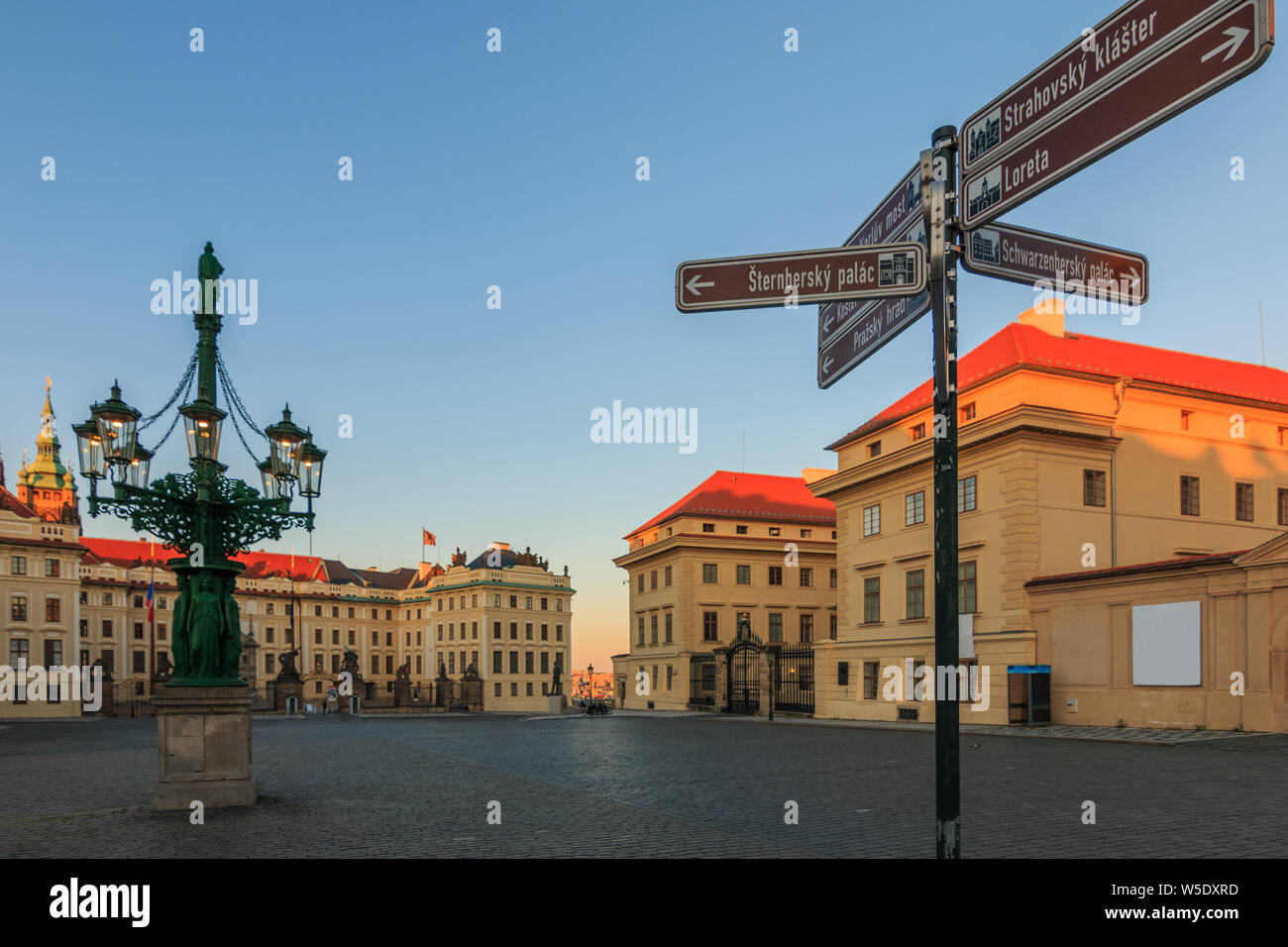 Hradcany Square in front of the entrance to Prague Castle with signs. Historically decorated fountain with the Schwarzenberg Palace in the evening in Stock Photo