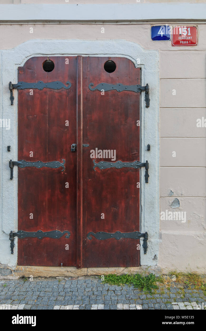 Historic closed wooden door on a building wall. Brown door with black metal fittings. bright wall with street sign and house number. walkway with pavi Stock Photo