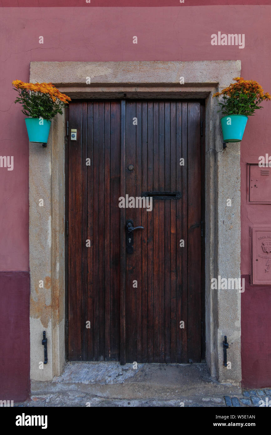 historic wooden gate of a residential house with flowerpots. Red and brown wall with granite slabs on the stage. closed wooden door with metal fitting Stock Photo