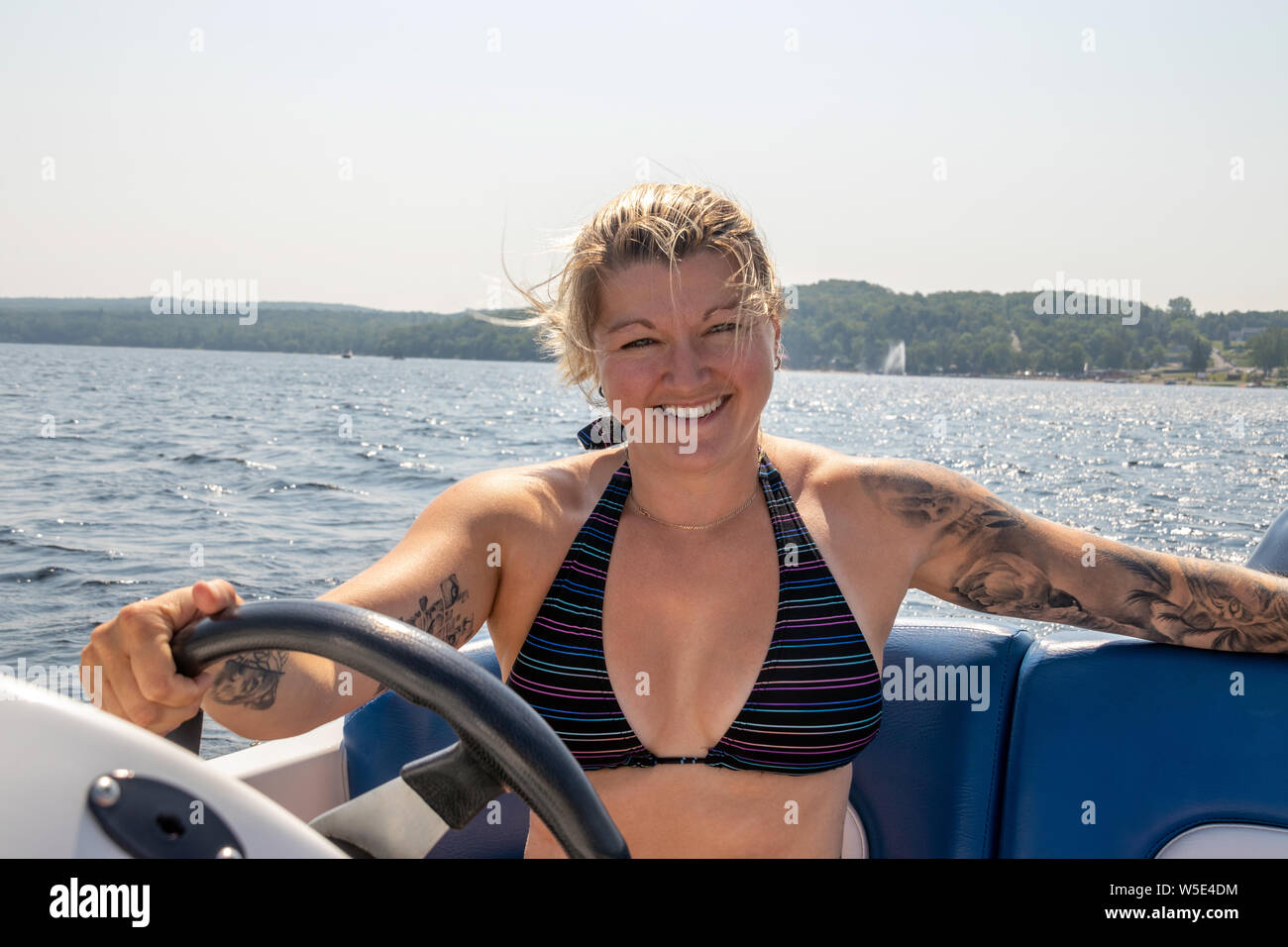Blond caucasian woman driving a sport motor boat on a lake at summer Stock Photo