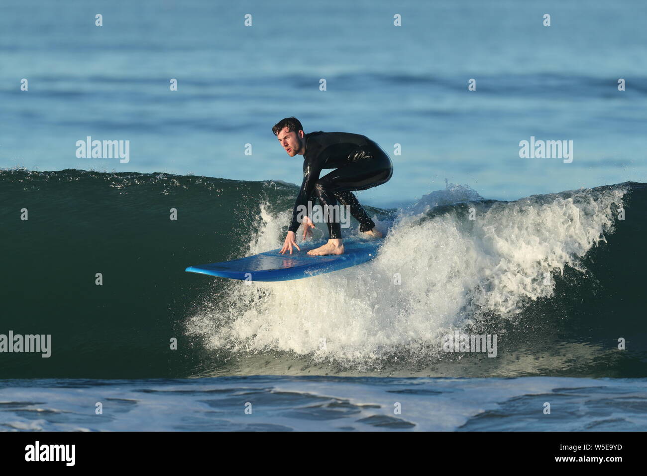Young man wearing a black wetsuit riding a blue surfboard in Huntington