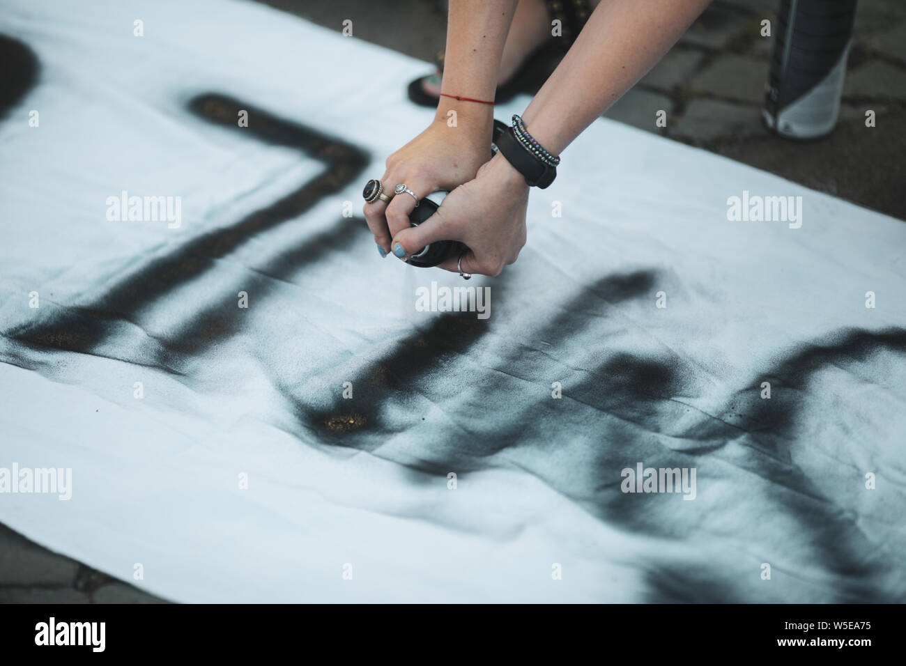 Details with the hands of a young woman writing with a black paint spray a feminist message on a piece of whitee cloth Stock Photo
