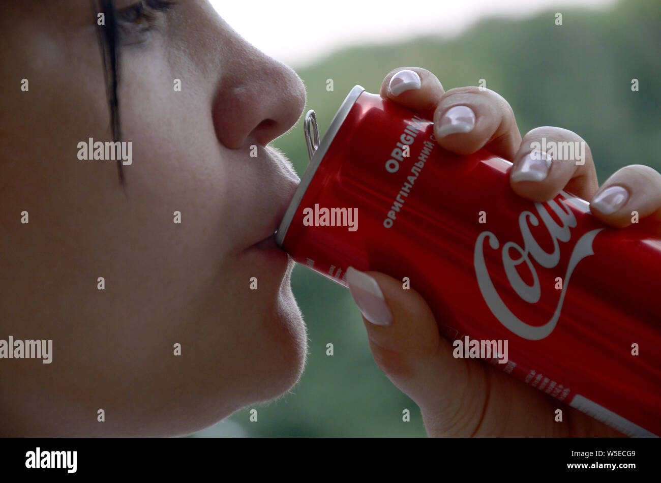 KHARKIV, UKRAINE - JULY 15, 2019: Caucasian brunette woman drinking coca cola bottle can 250ml in evening outdoors. Coca Cola is the most famous brand Stock Photo