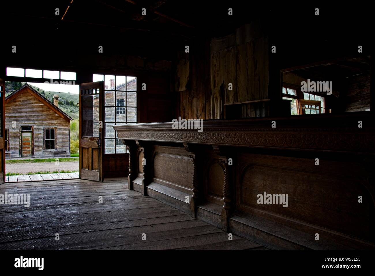 Natural lighting before a rainstorm; texture; wood floor and ornate, yet rustic wood bar in this western saloon with large window in Bannack, Montana. Stock Photo