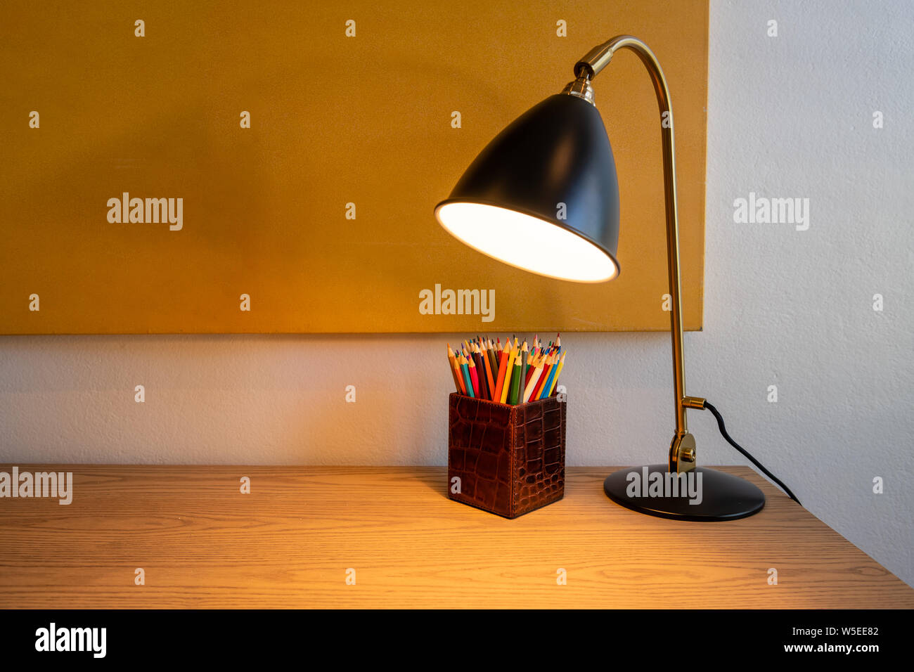 Desk lamp or light on an oak desk next to a wall with art work - box of ...