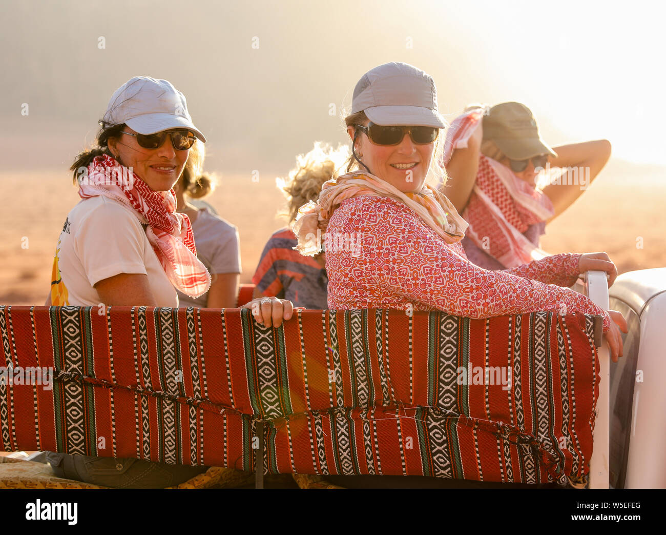 Women travel through Wadi Rum Jordan on cushions in the back of a pick up truck. Stock Photo