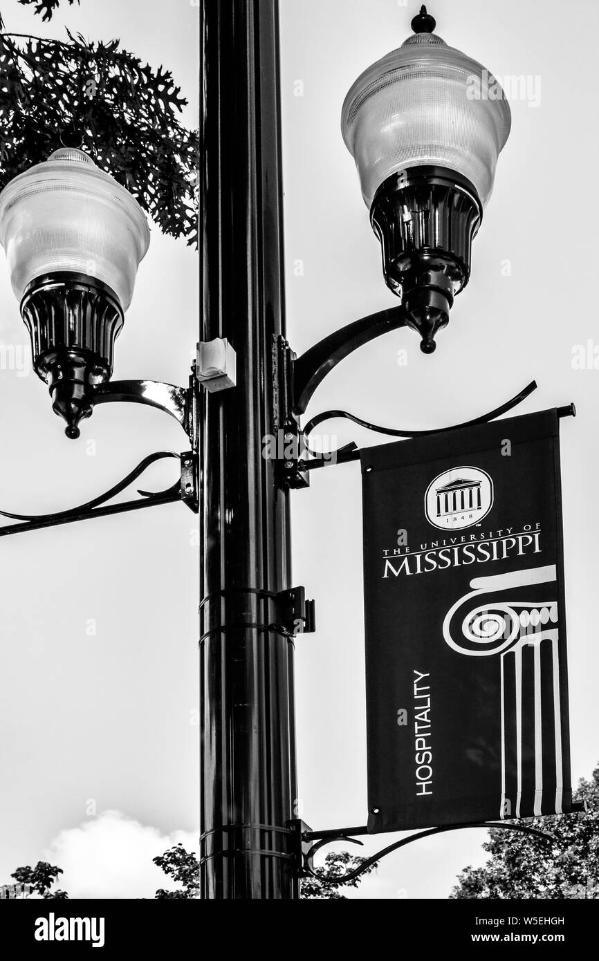 A University of Mississippi banner hangs from a vintage lamp post on the campus of Ole Miss in Oxford, MS, in black and white Stock Photo