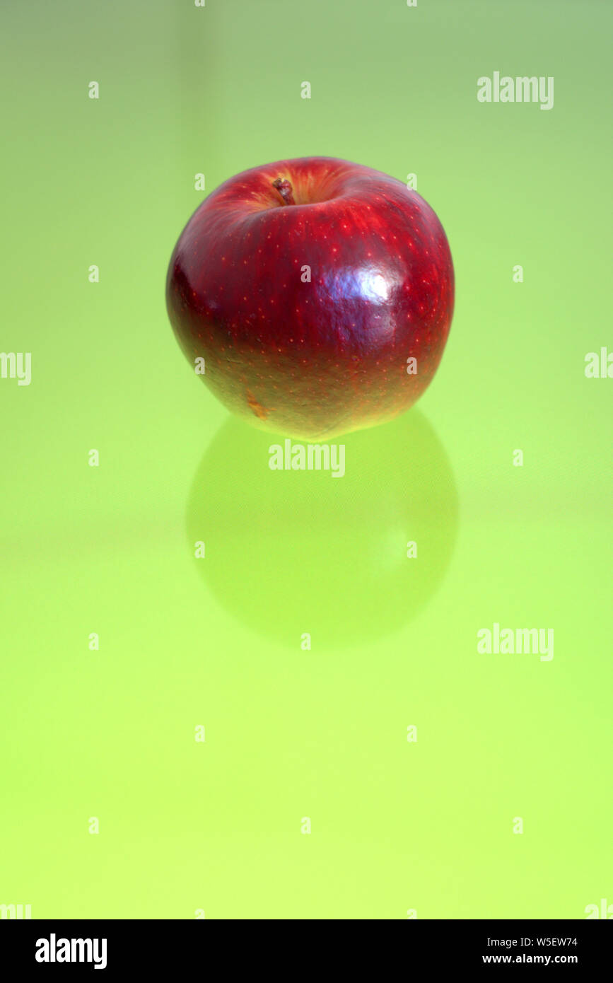 Red apple over a green reflective surface. Well suited for a concept background. Stock Photo