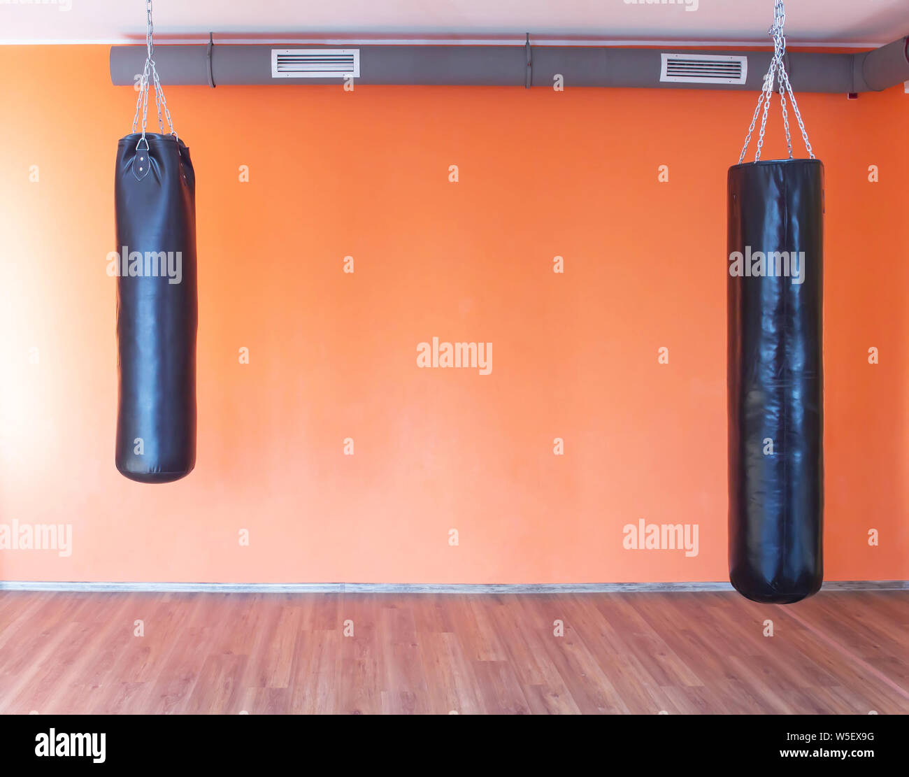 Punching bags for sports and martial arts hang in the gym against the background of the orange