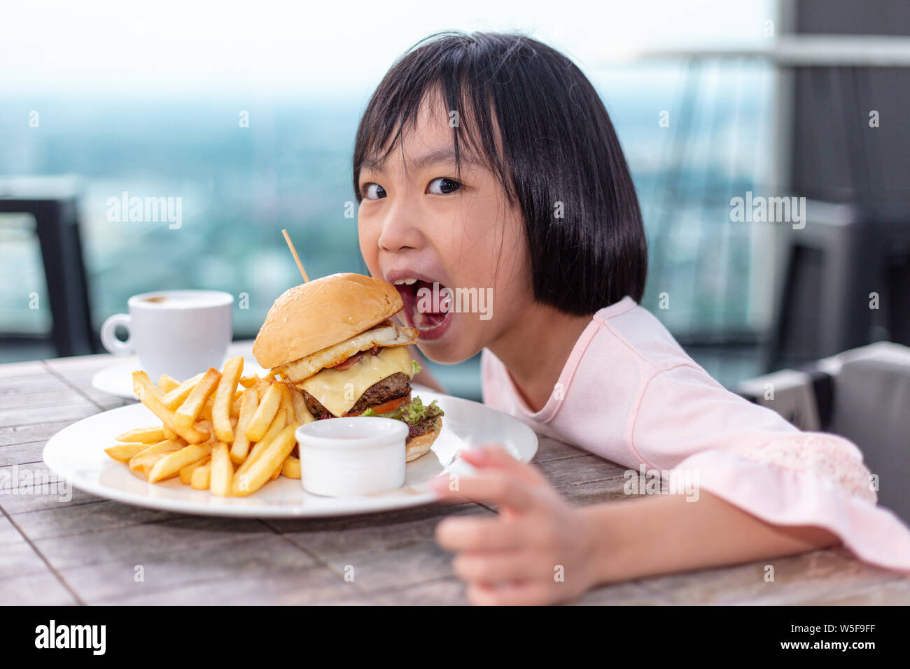 Asian Little Chinese Girl eating hamburger in the outdoor cafe Stock Photo