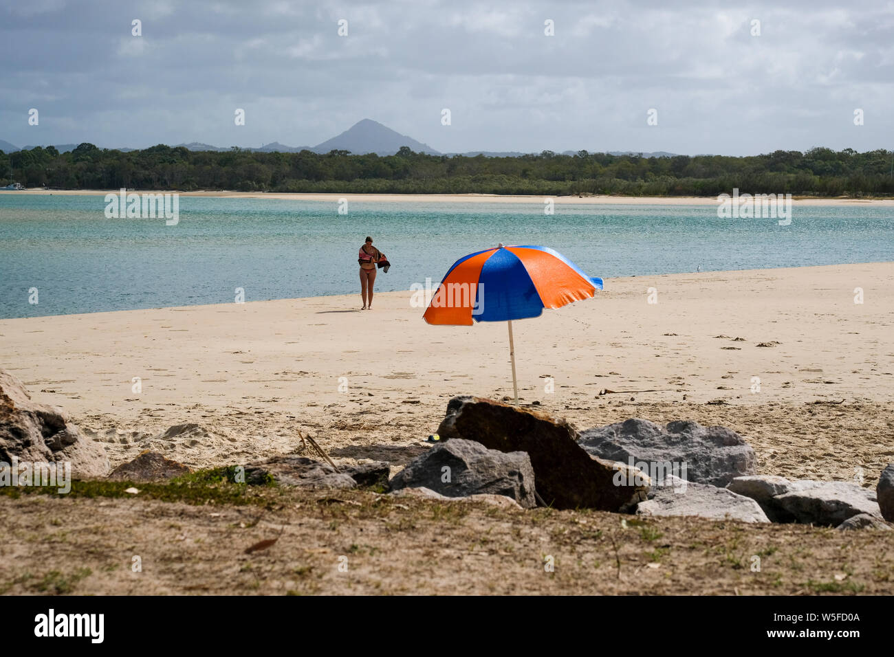 A swimmer emerges from the water on an isolated beach and returns to her beach umbrella Stock Photo