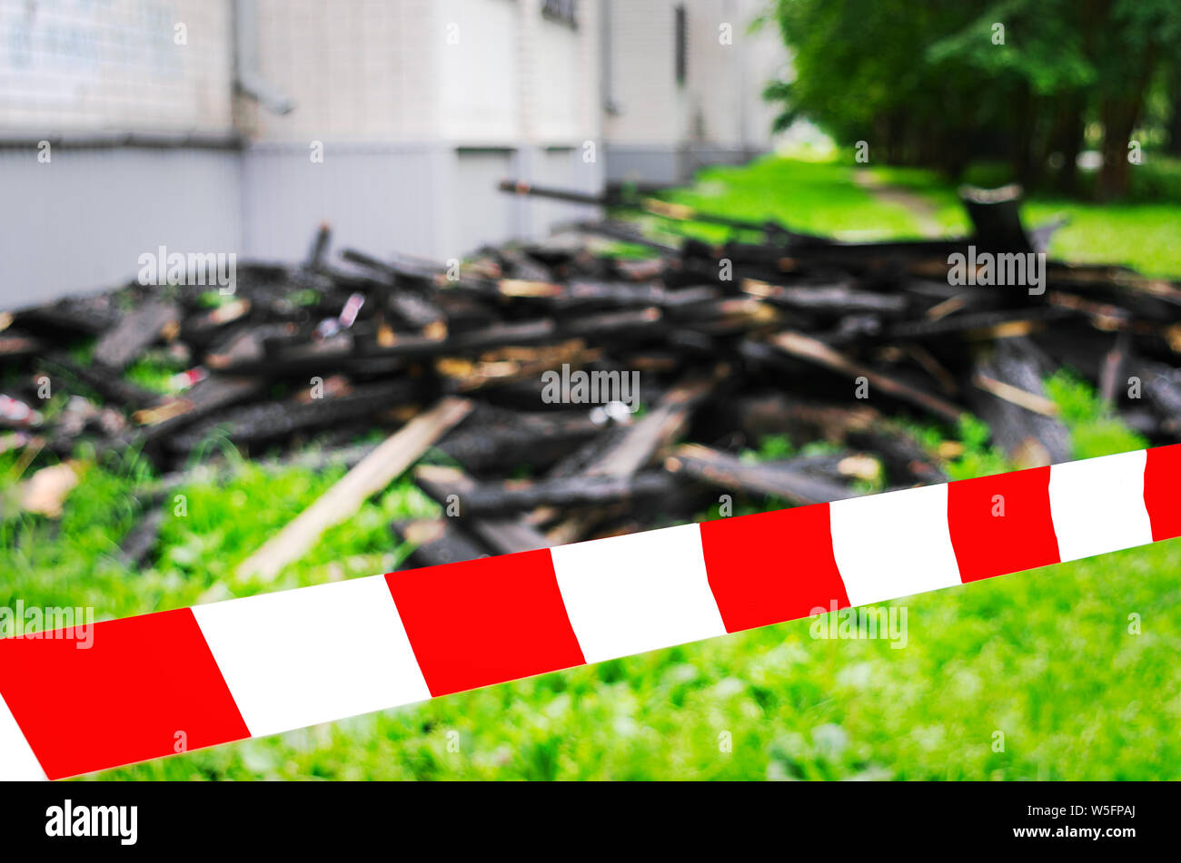 Red and White Safety Tape and Black Charred Rafters, Roof Framework on the Lawn near the Apartment Building after the Fire. Safety, Insurance Concept. Stock Photo