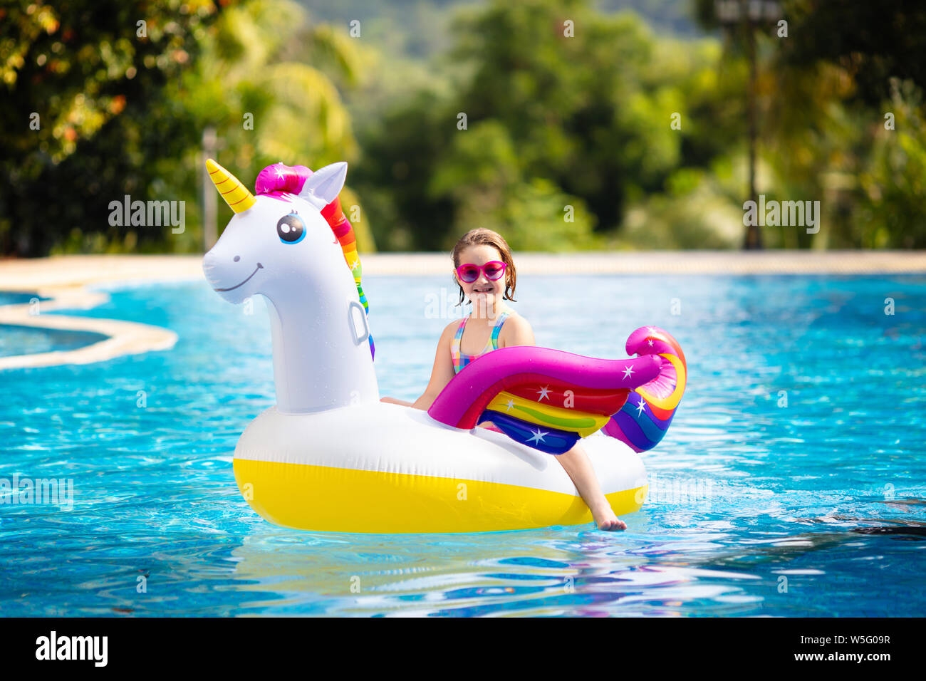 Child on unicorn float in swimming pool of tropical resort. Kids swim and play with inflatable